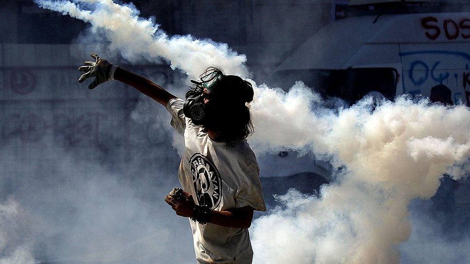 Демонстрант кидает обратно в сторону полицейских баллон со слезоточивым газом 