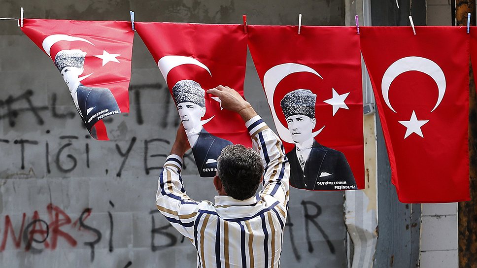 Мужчина развешивает флаги Турции с портретом Кемаля Ататюрка
