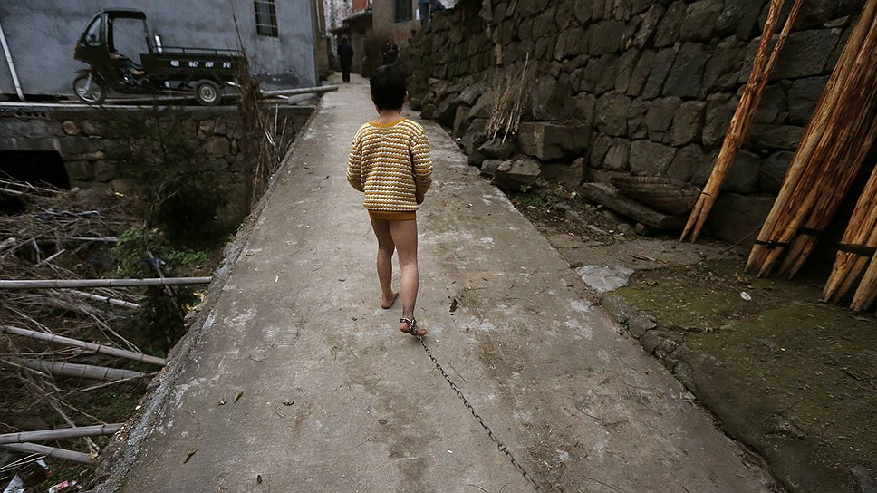 Одиннадцатилетний Хи Зили прогуливается на цепи возле своего дома в провинции Чжэцзян. В детстве ребенок  получил травму головы и начал страдать от психических расстройств 