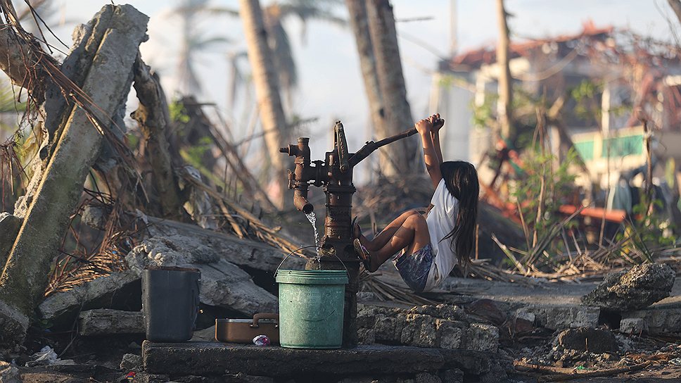 Ребенок, уцелевший после разрушительного тайфуна на Филиппинах, добывает воду с помощью ручного насоса