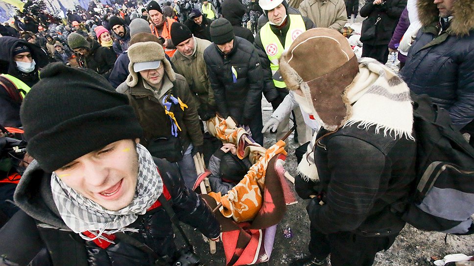 Участники митинга несут человека, которому стало плохо после ночного штурма на Майдане Незалежности