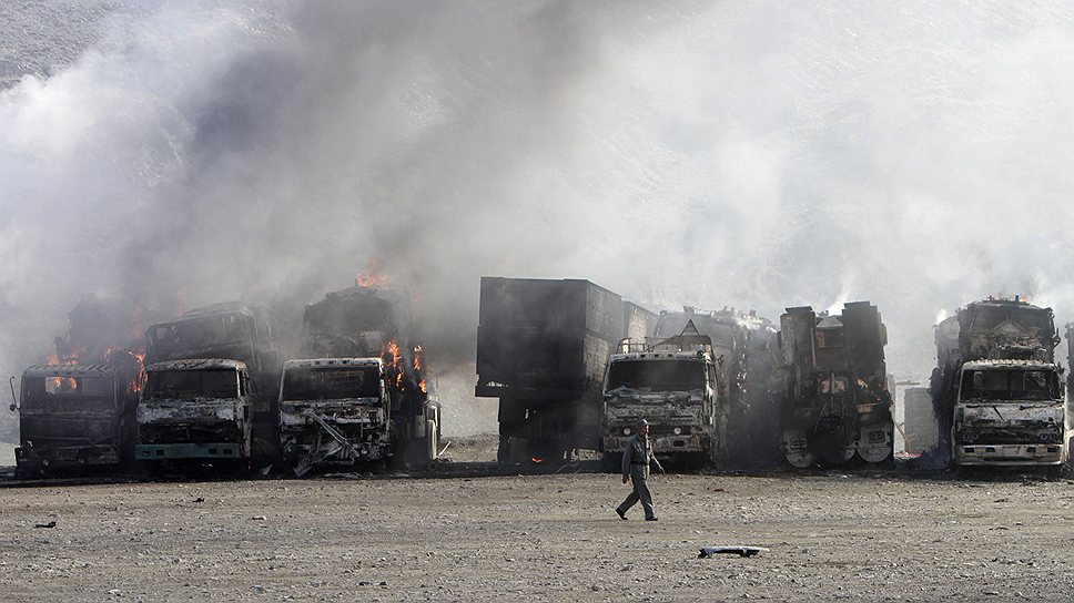 Афганский полицейский проходит мимо горящих грузовиков НАТО после нападения боевиков в районе  пакистано-афганской границы
