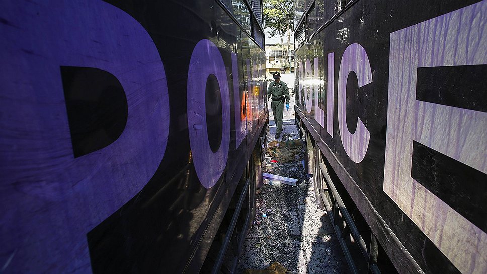 Сотрудник службы безопасности осматривает разбитые полицейские грузовики на стадионе в Бангкоке, который стал местом ожесточенных столкновений между полицией и протестантами