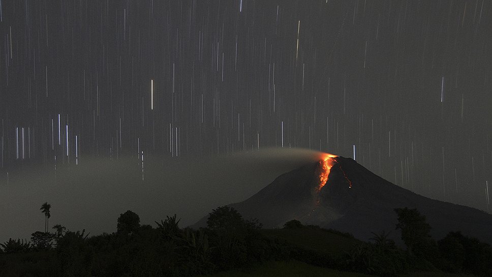 Вулкан Горы Синэбанг, извергающий ночью горячую лаву. Деревня Йрая в районе Каро, Индонезия 