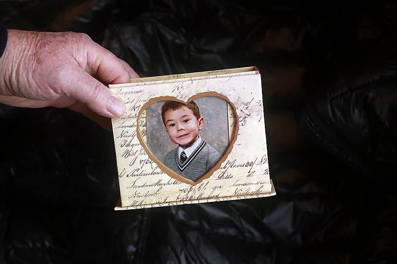 67-летняя Мигель Эвери держит фотографию своего внука, которому тяжело покинуть затопленный дом из-за синдрома Аспергера и эпилепсии