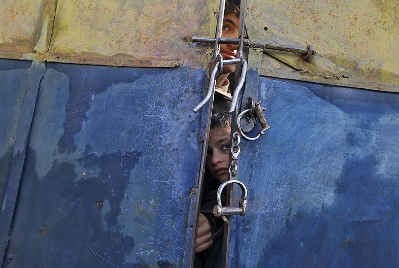 Индийские дети смотрят на тела предполагаемых боевиков через щель в воротах полицейского участка в Лалпоре