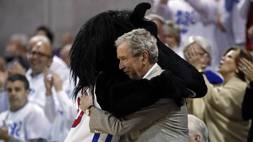 Бывший президент США Джордж Буш обнимается с талисманом баскетбольной команды SMU во время перерыва в матче с командой Луисвилля в Далласе