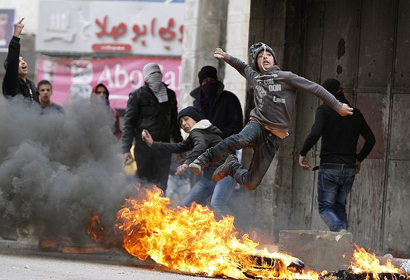 Юный палестинец кидает камень в израильских солдат в городе Хеброн на Западном берегу Иордана