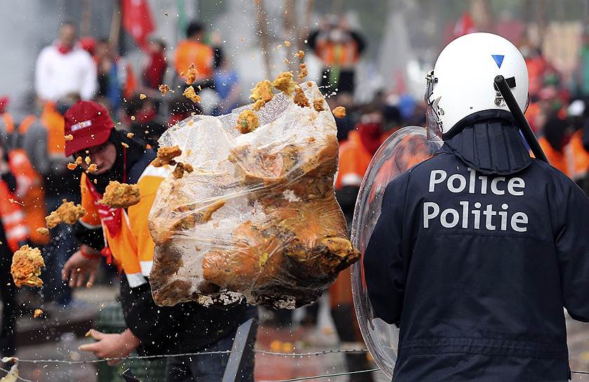 Демонстрант кидает пакет с мусором в полицейского во время акции протеста европейских профсоюзов в Брюсселе