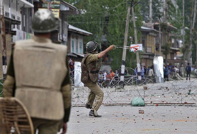 Индийский полицейский кидает камень в участников акции протеста против выборов в Шринагаре