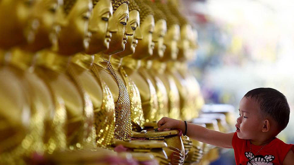 Ребенок кидает монеты в золотые статуи Будды в честь праздника Весак в Куала-Лумпур, Малайзия