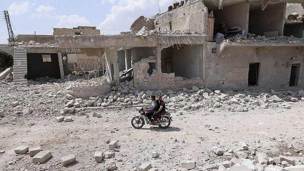 Местные жители едут на мотоцикле среди развалин Алеппо