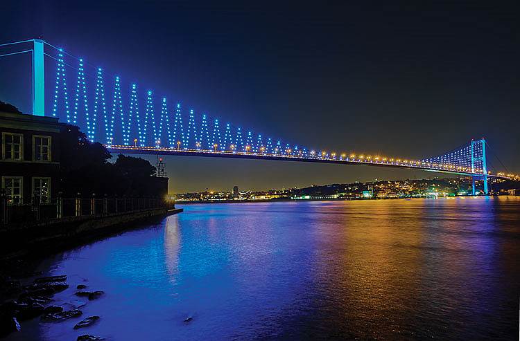 Босфорский мост, висячий мост через Босфорский пролив, соединяющий европейскую и азиатскую части Стамбула, составляет 1560 метров в длину. Задачей Philips в данном проекте стало освещение трех основных компонентов моста — башен, зигзагообразных стальных кабелей и поручней — с помощью светодиодных решений Philips Color Kinetics. Башни, чья высота достигает 105 метров, освещены прожекторами ColorReach Powercore с равномерно интенсивным светом. Вдоль ограждений были установлены светильники iColor Accent Powercore, излучающие прямой динамический свет с изменяющимся цветом. Находясь на пике каждого зигзага, прожекторы ColorBlast Powercore светят как яркие белые точки, подчеркивая очертания всей конструкции моста и усиливая его привлекательность&lt;br>Bosphorus Bridge, Стамбул, Турция
