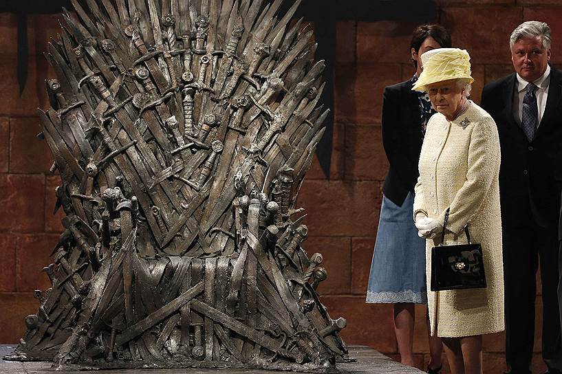Королева Великобритании Елизавета II осматривает Железный Трон во время встречи с актерами сериала «Игра престолов» на съемочной площадке в Белфасте