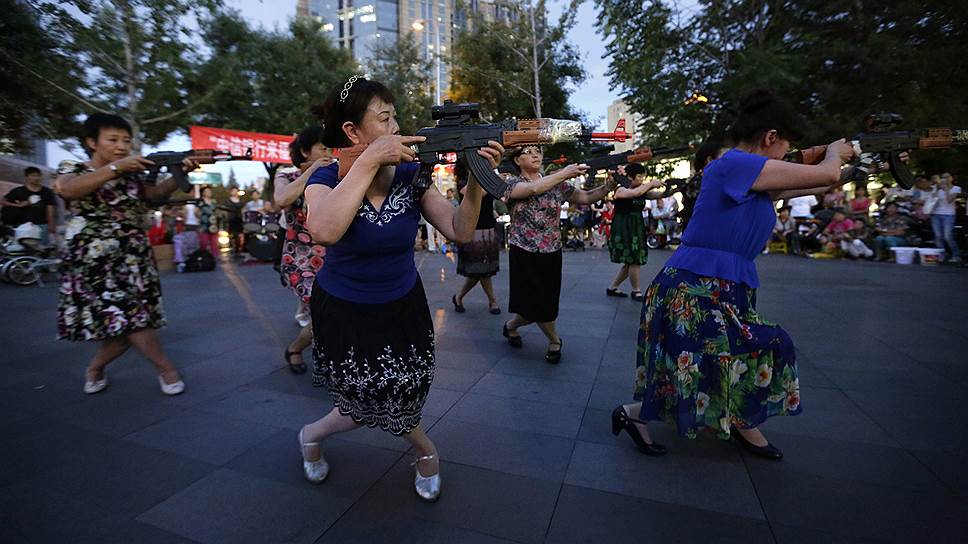 Китаянки с игрушечными автоматами во время патриотического танца, являющегося частью их ежедневной фитнес-программы, на одной из площадей в Пекине