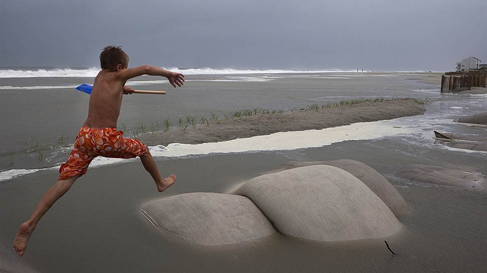 Побережье Огайо. Мальчик прыгает через мешки с песком, установленные для борьбы с эрозией пляжа после урагана