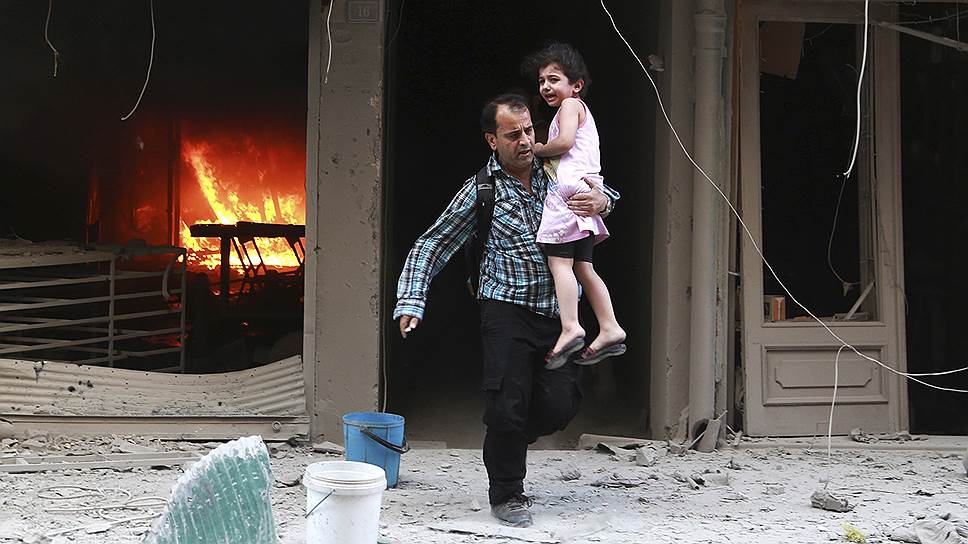 Мужчина с ребенком спасаются из здания, загоревшегося, по словам повстанцев, в результате попадания бомбы, выпущенной сирийскими военными, в Алеппо