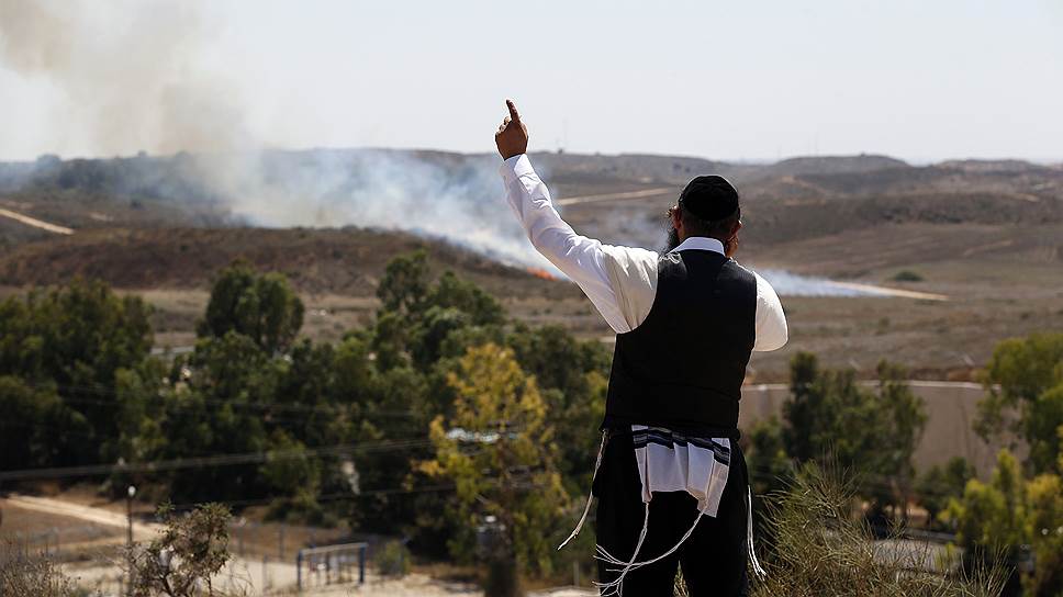 Ортодоксальный иудей говорит по мобильному телефону, глядя на пожар, возникший после попадания ракеты, в городе Сдерот