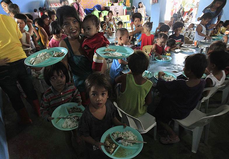 Дети из трущоб Манилы, Филиппины, держат тарелки с едой, которую им раздали волонтеры