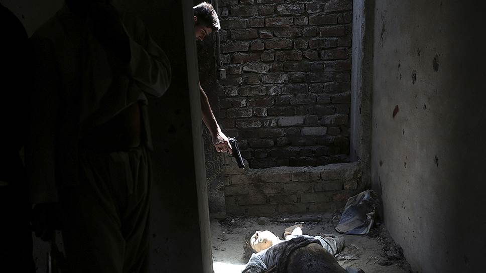 Местный житель направляет пистолет на труп боевика в доме, где ранее — до нападения на них — размещалась группа боевиков (Кабул, Афганистан)
