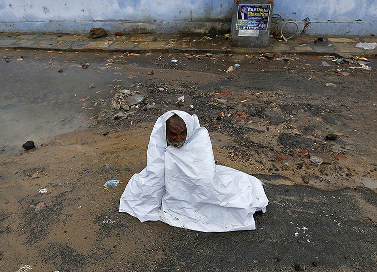 Индийский мужчина, укрывающийся от дождя пластиком на улице в Ахмедабаде