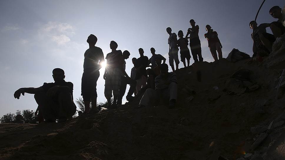 Палестинцы наблюдают за работой спасателей, ищущих людей под завалами дома в Рафахе, разрушенного в результате израильской атаки