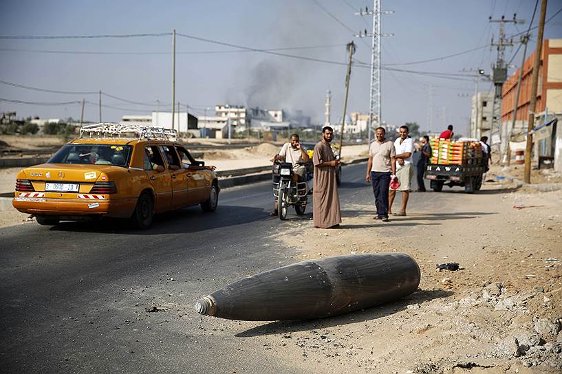 Палестинцы смотрят на неразорвавшийся снаряд в Газе