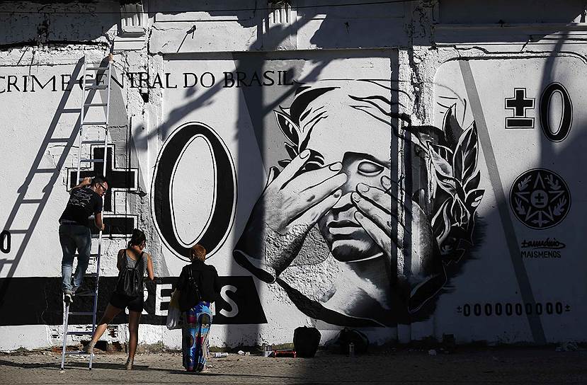 Люди стоят перед граффити на стенах, высмеивающем бразильскую валюту, в центре Рио-де-Жанейро