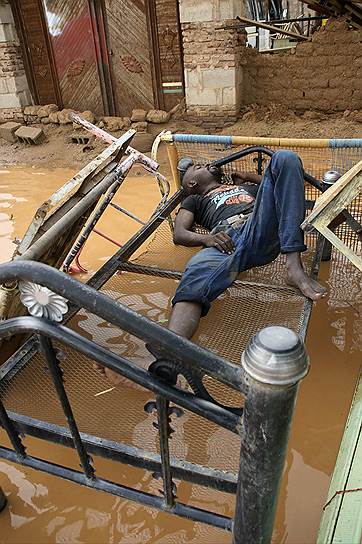 Человек перед домом, поврежденным паводком в Судане
