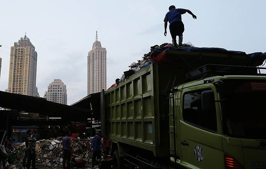 Рабочий на вершине грузовика с мусором на продовольственном рынке в Джакарте, Индонезия
