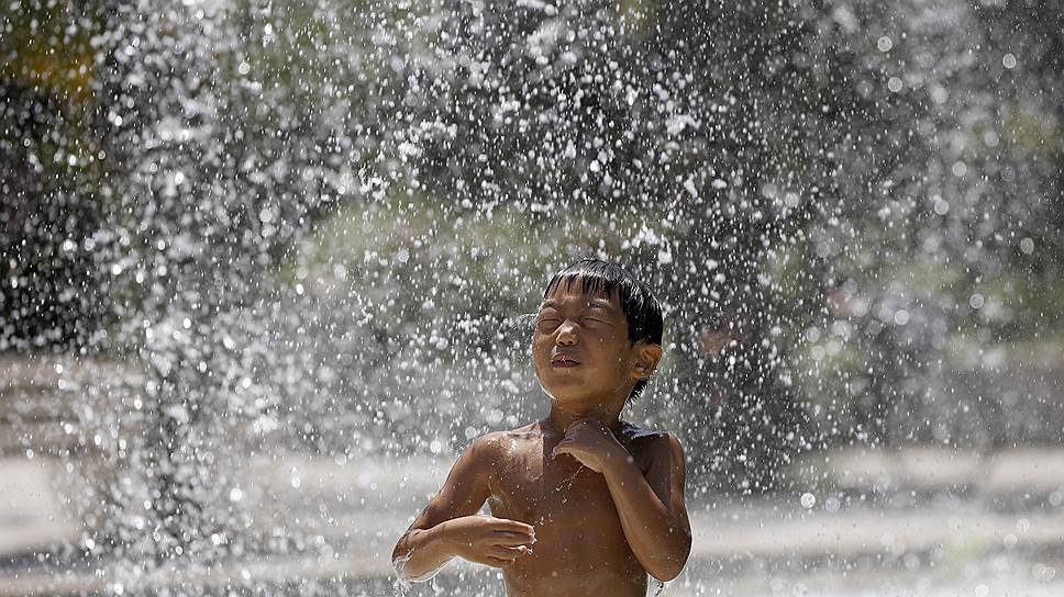 Мальчик спасается от жары в фонтане в парке Токио