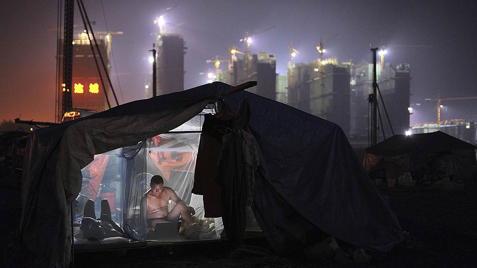 Рабочий сидит с ноутбуком в своей ночлежке рядом со строящимся жилым комплексом в в Хэфее (Китай)