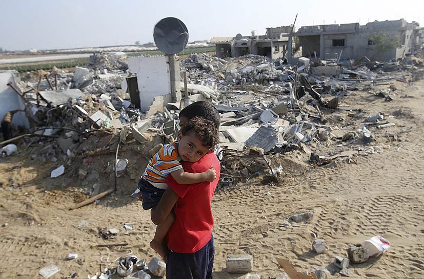 Палестинский мальчик несет своего брата возле дома, разрушенного израильской авиацией в Хан-Юнисе, сектор Газа