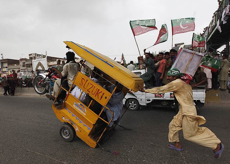 Сторонник пакистанского оппозиционного политика Имрана Хана помогает перегруженному рикше вернуть переднее колесо на землю во время Марша свободы в Гуджрате