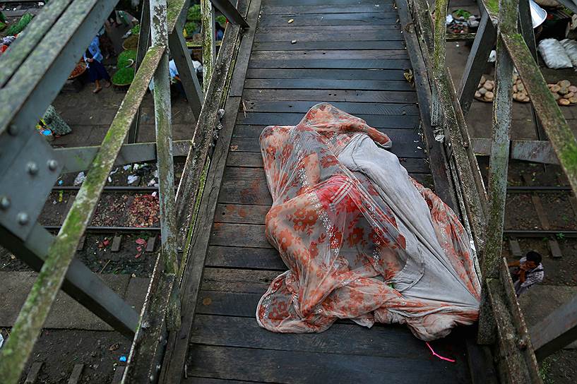 Мужчины, укрытые противомоскитной сеткой, спят на мосту над железнодорожной станцией в Янгоне, Мьянма