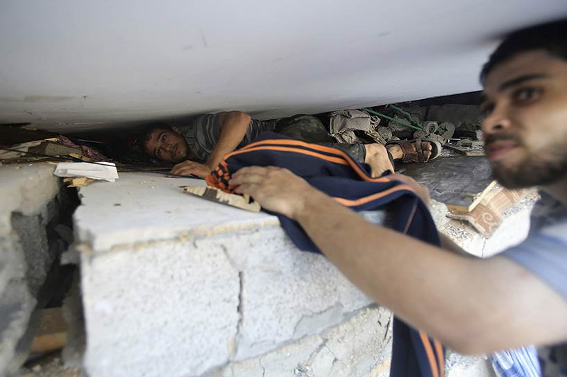 Палестинец ищет вещи под обломками своего дома, уничтоженного во время израильского авиаудара