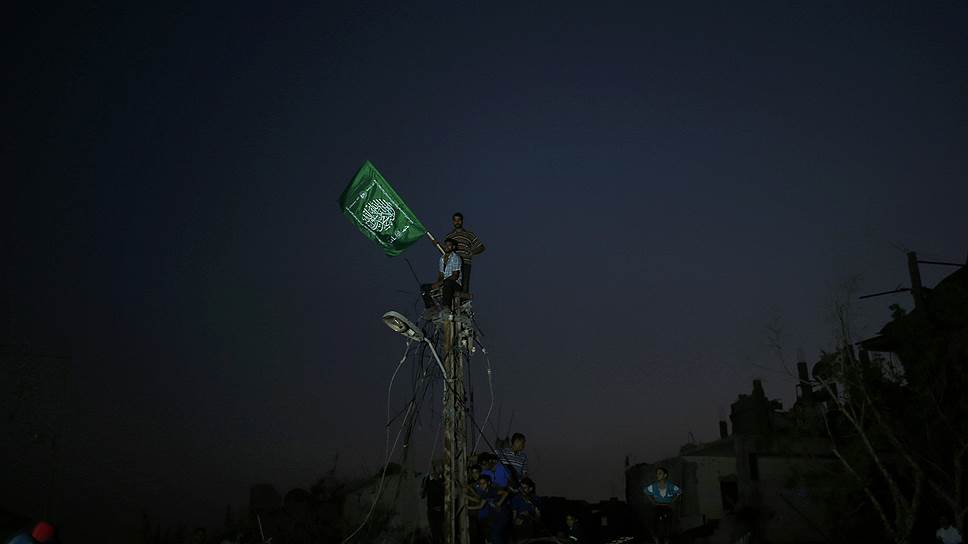 Палестинцы со своим флагом взобрались на электрический столб после того, как напряжение было отключено в ходе израильского наступления восточнее Газы