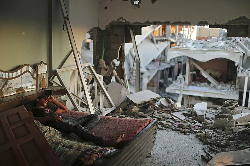 Палестинец спит на кровати в разрушенном доме в Бейт-Хануне в секторе Газа