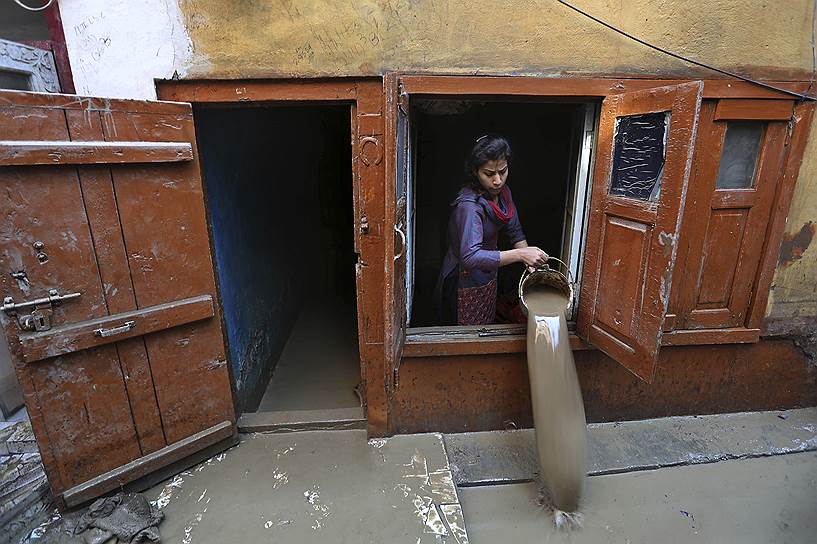 Жительница Шринагара выливает воду из своего дома после наводнения