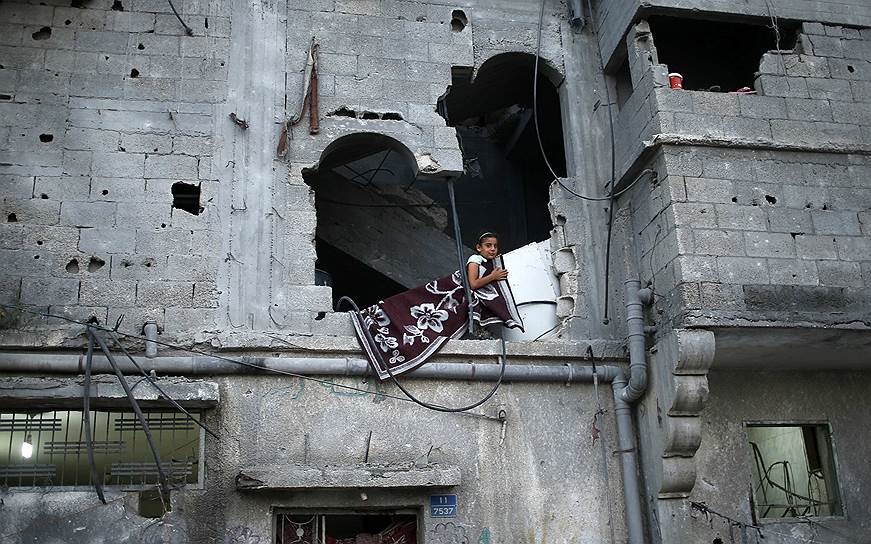 Палестинская девочка выглядывает из окна своего дома в Газе, частично разрушенного во время войны с Израилем
