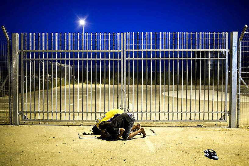 Мигранты из Африки молятся возле ворот центра для задержанных нелегалов в израильской пустыне Негев, который по решению Верховного суда Израиля должен быть закрыт в ближайшее время
