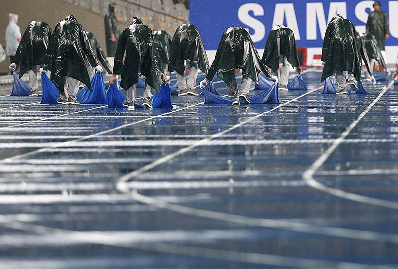 Работники стадиона пытаются высушить беговые дорожки перед финальными забегами на 100 м в рамках 17-ых Азиатских игр