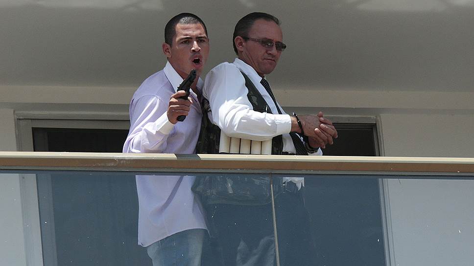 Неизвестный мужчина (слева) на балконе отеля Saint Peter в Бразилии угрожает пистолетом сотруднику отеля, которого заставил надеть жилет, якобы начиненный взрывчаткой