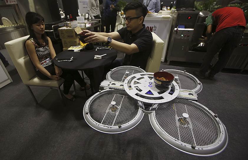 Посетители Национальной продуктовой выставки в Сингапуре, которых обслуживает беспилотный летательный аппарат, выполняющий функции официанта