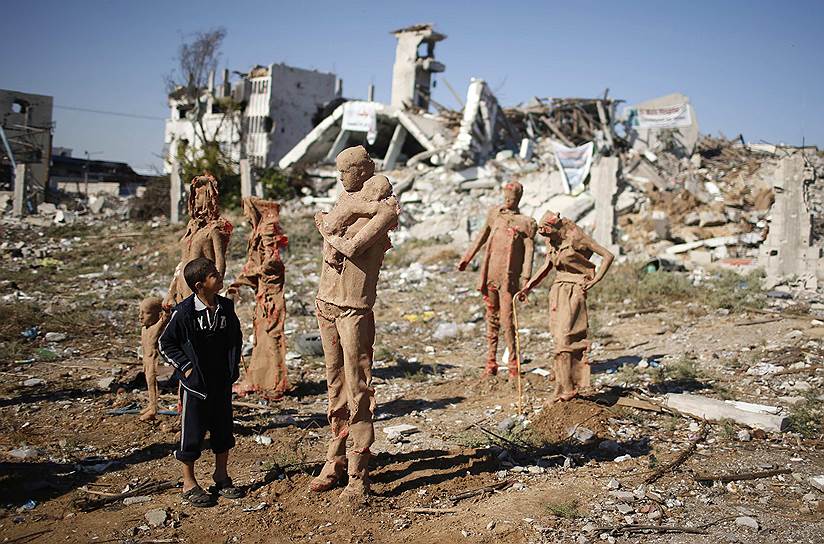 Мальчик рассматривает статуи на улице в Газе, изображающие палестинцев, покинувшие свои дома в результате войны с Израилем