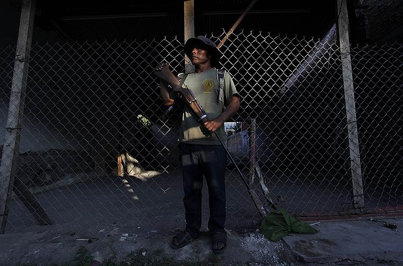 Дружинник стоит на страже, пока его товарищи передают властям подозреваемого в изнасиловании нескольких детей в мексиканском городе Акатемпа