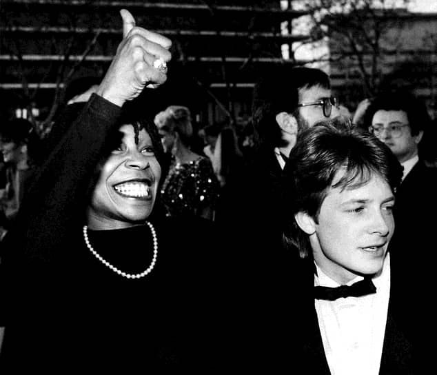 Дебют Вупи Голдберг в кино был высоко оценен критиками и зрителями. Она получила номинацию на «Оскар» и была отмечена «Золотым глобусом»
&lt;br>На фото: с актером Майклом Джей Фоксом на церемонии вручения премии «Оскар» в 1986 году
