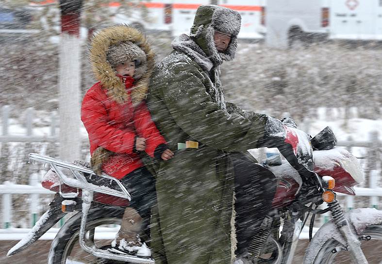 Баликун, Китай. Мотоциклист с ребенком едет во время снежной бури