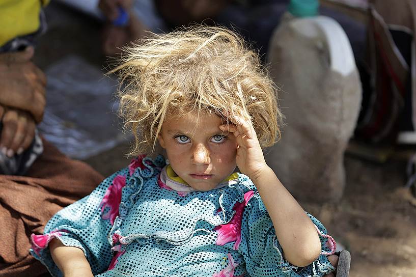 Девочка из группы езидов, которая пытается сбежать из Ирака вместе с семьей, спасающейся от преследования боевиками ИГИЛ
&lt;br>Юсеф Боудлал: «Я очень хорошо помню этот момент. Это было в тот день, когда я доехал до иракско-сирийской границы. Шокированные, сгорающие под солнцем мужчины, женщины и дети в грязной и рваной одежде пытались справиться с 45-градусной жарой. Сначала я обратил внимание на группу женщин, сидящих на земле, но затем, обернувшись, увидел маленькую девочку. Я сфотографировал ее, и в этот момент она посмотрела на меня и улыбнулась. Я сделал еще один снимок ее вместе с матерью. Я был обескуражен ее красотой. Было столько силы и грусти в ее глазах. Здесь были сотни таких грязных, измученных детей и матерей, и от этого становилось грустно. Но я все время думаю об этой девочке, о том, что будет с ней и со всеми остальными»