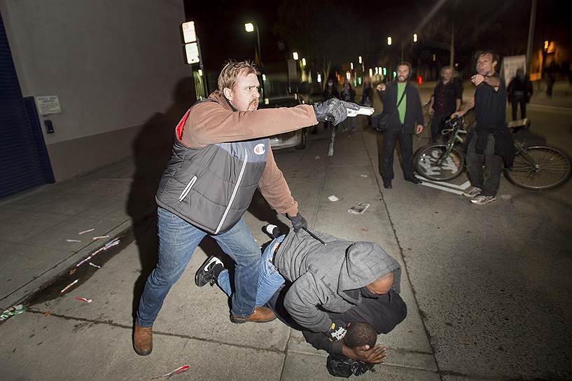 Окленд, Калифорния, США. Офицер полиции, работающий под прикрытием, отбивается от демонстрантов, протестующих против полицейского произвола